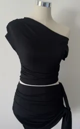 Top corto negro con un hombro descubierto y frunce lateral.