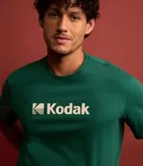 Remera blanca de algodón con cuello redondo y mangas cortas. Estampa frontal con el logo de Kodak en azul.