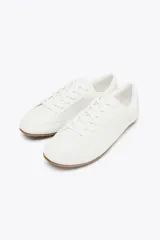 Zapato deportivo tipo blucher color blanco con suela marrón.