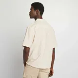 Camisa de manga corta color beige claro, con cuello clásico y cierre frontal con botones. Confeccionada en mezcla de lino.