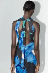 Vestido largo de tejido fluido con estampado floral azul sobre fondo negro. Tiene cuello subido con frunces y lazada, espalda descubierta, forro interior y abertura lateral en el bajo.