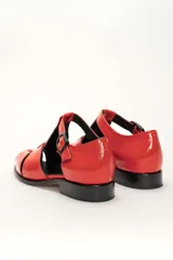 Sandalia roja de cuero vacuno con diseño de tiras entrecruzadas y hebilla lateral. Tiene suela de cuero artesanal y taco bajo.