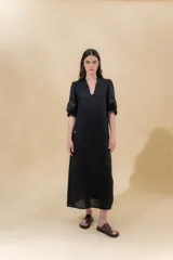 Vestido largo color beige, confeccionado en lino, con escote en V con volados y apliques de puntilla en las mangas. Posee bolsillos delanteros y tajos laterales.