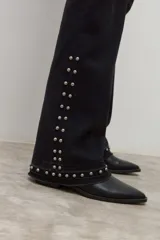 Jean negro de tiro medio, corte bootcut, con tachas metálicas plateadas decorando los laterales de las piernas y el ruedo.