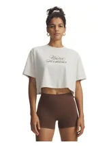 Remera corta (crop top) de manga corta, color blanco hueso, con el logo de Under Armour estampado en el pecho en tipografía cursiva de color marrón.