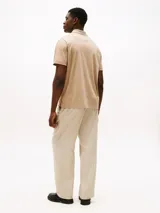 Chomba color beige con patrón integral de logos bordados, cuello tipo chomba, cartera de dos botones, corte clásico y manga corta.