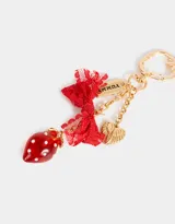 Llavero metálico dorado con dije de frutilla roja con incrustaciones blancas, moño de encaje rojo, dije con la palabra "Yummy!" y dije de corazón alado.
