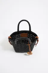 Bolso tipo tote de mimbre color marrón oscuro, con doble asa corta y correa de cuero marrón. Incluye dije circular dorado con letras grabadas.