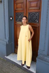 Vestido amarillo de corte amplio, largo midi, con escote redondo, sin mangas, bolsillos laterales y logo bordado en el frente.