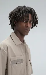 Camisa beige de manga corta, estilo técnica, confeccionada en microfibra liviana. Con doble bolsillo frontal y broches en lugar de botones.