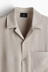 Camisa de manga corta color beige con cuello abierto, tapeta lisa, bolsillo superior y bajo recto. Corte estándar para una silueta clásica y cómoda.