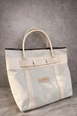 Bolso de playa de lona color verde claro con detalles en cuero color beige. Tiene doble asa de hombro y cierre superior con tira de cuero.