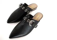 Mulas negras de cuero texturizado con punta afilada, abertura central, tira ajustable con hebilla plateada y mini taco plateado de 1,5 cm.