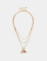 Collar corto dorado compuesto por tres cadenas de diferentes diseños: una de eslabones finos, una con perlas irregulares y otra de eslabones más grandes. Presenta dijes de frutas con strass de colores.