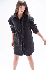 Camisa larga negra de poliéster con textura de pana fina, con mangas largas y cierre frontal con botones. Presenta volados verticales en el frente.