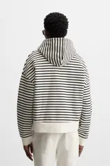 Sudadera con capucha a rayas horizontales blancas y negras, corte boxy fit, mangas largas y texto bordado en color rosa en el pecho.