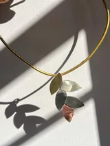 Gargantilla rígida dorada con dije de cinco hojas de diferentes metales: alpaca, bronce y cobre.