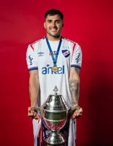 Camiseta de fútbol Umbro del Club Nacional de Football, modelo Home 2025. Diseño blanco con detalles en azul y rojo en cuello y mangas. Incluye logo de Umbro, escudo del club y sponsor Sarubbi en el frente.