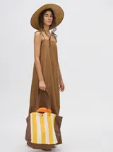 Vestido midi de denim algodón color marrón, con escote recto y tirantes finos ajustables con lazos. El corte es suelto y termina con un ruedo con semi-volado.