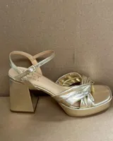 Sandalia de cuero vacuno color dorado, con plataforma y taco cuadrado. Presenta una tira delgada en el tobillo y detalle de nudo en la capellada.