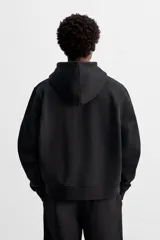 Sudadera negra relaxed fit de algodón compacto con interior en rizo, cuello con capucha ajustable, manga larga, bolsillos frontales tipo canguro, acabados en rib y cierre frontal con cremallera.
