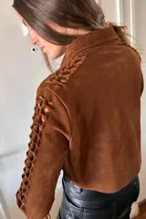 Camisa marrón de gamuza con cuello clásico, cierre con botones a presión y mangas largas con detalles artesanales calados.