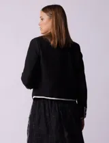 Chaqueta de tweed blanca con ribete negro, escote a la base, abertura central con botones, bolsillos delanteros y puños con aplique de botones perlados.