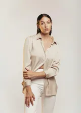 Camisa color beige claro de satén con cuello clásico, mangas largas con puños abotonados y cierre frontal con botones.
