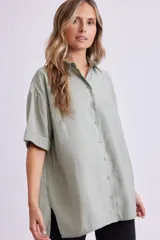 Camisa verde de corte holgado, con cuello clásico, cierre frontal con botones y mangas cortas con dobladillo.