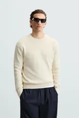 Jersey color crema de punto perlado, con cuello redondo, manga larga y corte regular fit.