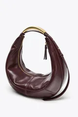 Bolso ovalado color borgoña de cuero sintético, con asa de hombro metálica dorada y cierre de cremallera.