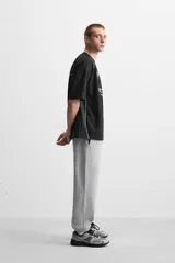 Camiseta negra de corte boxy fit, cuello redondo y manga corta. Presenta logos estampados en blanco en el frente y detalles en verde en los laterales.