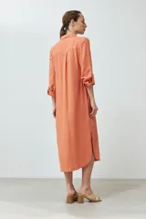 Vestido camisero midi color durazno, de lino, con cuello camisero, abotonado al frente y mangas largas con trabillas.