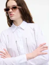 Camisa blanca de algodón con cuello camisero, cierre frontal con botones y apliques de cadenas plateadas.