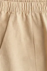 Pantalón color beige de lino con tiro alto, cintura elástica, bolsillos al bies y bolsillos traseros insertados. Piernas rectas con pliegue cosido adelante.