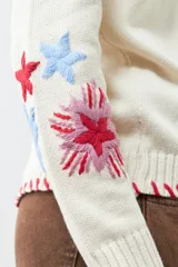 Cárdigan color crema con botones, ribete rojo y bordados de flores y mariposas en las mangas.