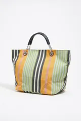 Bolso tote de tela a rayas verticales en tonos verde oliva, lila, blanco y rosa. Tiene doble asa de mano de cuero marrón y logo de la marca en etiqueta de cuero.