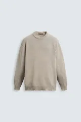 Jersey de punto color beige, con cuello redondo, manga larga y corte holgado. Presenta un lavado con efecto desgastado y rotos en toda la prenda.