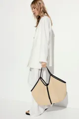 Bolso shopper de paja de plástico trenzada color beige con detalles en tejido revestido negro. Asas estrechas, correa fina en la parte superior y bolsillo interior con cierre.