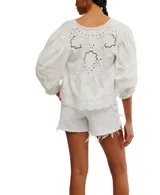 Blusa blanca de algodón con escote en V, mangas globo 3/4 con detalles de encaje y puños elásticos. Presenta lazos en el frente para atar.