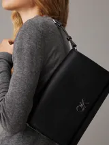 Cartera de hombro negra de cuero sintético con correa ajustable y cierre giratorio. Incluye bolsillo exterior trasero y compartimentos interiores con cremallera.