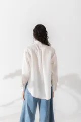 Camisa marrón de lino con cuello mao con volados, manga larga, cierre frontal con botones y bolsillo pequeño en el pecho.