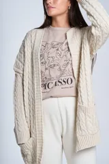 Saco tejido color crema con diseño de ochos y bolsillos frontales.