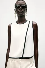 Blusa blanca sin mangas de crepe con cuello redondo y detalle de ribete negro en cuello, sisas y abertura frontal diagonal.