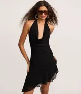 Vestido corto negro de tejido liviano, con escote halter que forma un drapeado (escote degagê) en el busto y ruedo asimétrico con volados.
