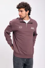 Buzo deportivo marrón con cuello alto y medio cierre frontal con cremallera. Tiene logo bordado en el pecho y puños y cintura acanalados.