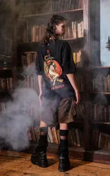 Remera negra de manga corta con cuello redondo y calce oversize. Presenta una estampa en la espalda inspirada en el tarot, con la carta "La Fuerza" que muestra a una mujer desnuda sobre un leopardo, rodeada de vegetación y un sol rojo.