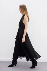 Vestido largo negro de viscosa georgette, con caída fluida y lazo trenzado en la cintura. Presenta doble capa en la parte superior que combina recortes y transparencias.