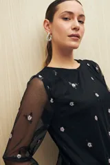Blusa negra de tul bordado con pequeñas lentejuelas y mangas largas transparentes.