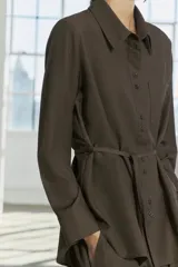Camisa marrón de Zara Woman Collection, confeccionada en hilatura con viscosa. Tiene cuello solapa, manga larga con puño, bolsillo de plastrón en el pecho, cinturón ajustable con lazadas y bajo asimétrico. Se cierra con botones frontales.